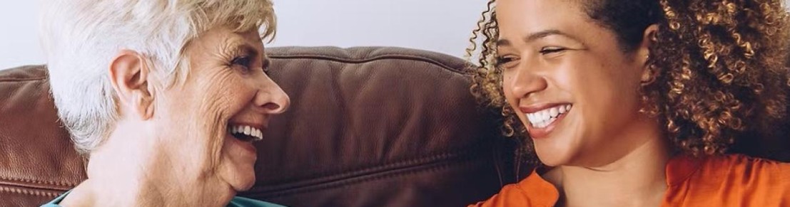 two homesharers sit on a sofa smiling at each other