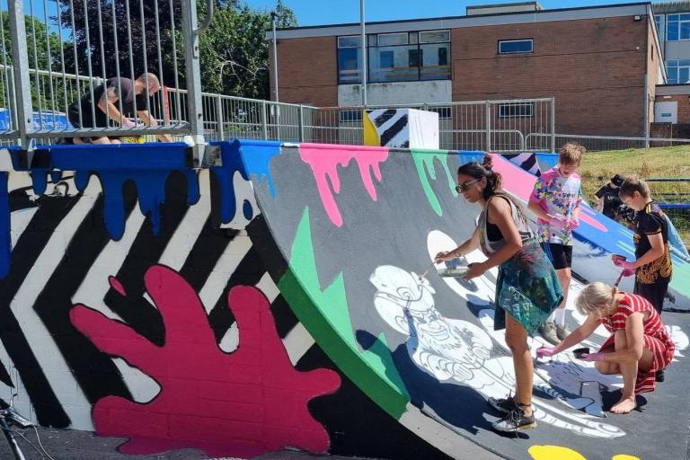 Volunteers paint a vibrant mural onto a skatepart ramp