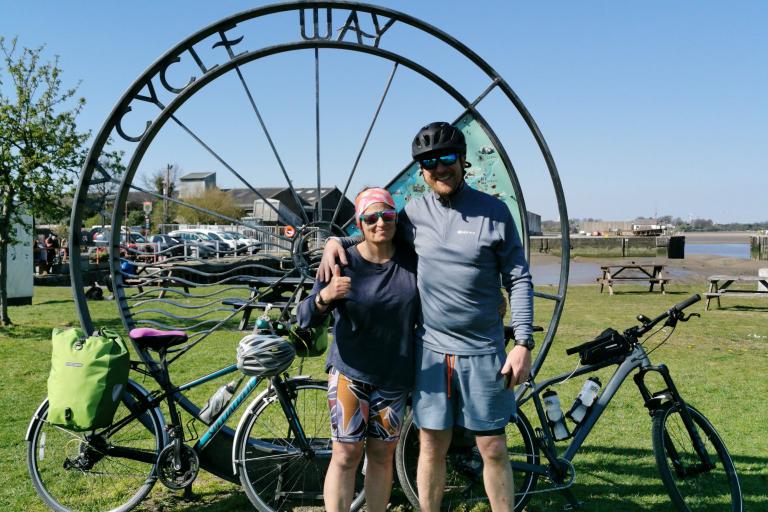 Two people standing in front of a cycle route sculpture, their bikes behind them.