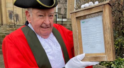 Town crier in traditional dress holding the proclamation in a wooden case