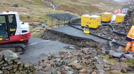 A section of road at Kirkstone Pass with a trench dug out of it and a digger.