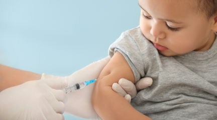 A toddler receiving a vaccine in the right arm from a health professional