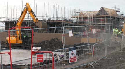 A building site with two house being built in the background and a digger in the foreground