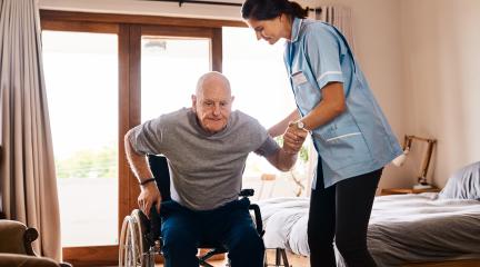 A carer helping an old man into a wheelchair