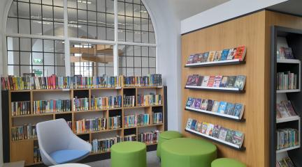 Seating area of Kendal Library with shelves of books and a big arched window