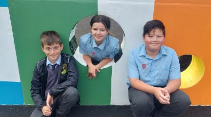 Three children in front of a football wall, a brightly coloured wall with holes for kicking a football through..