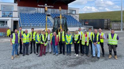 A line of people in yellow high-viz jackets standing in front of seats at a football ground.