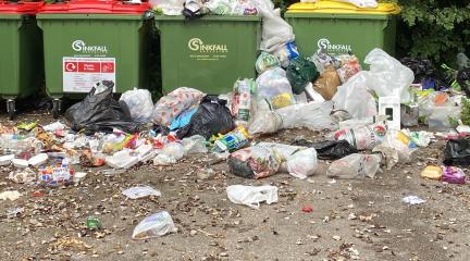 Rubbish piled up and strewn in front of green recycling banks.