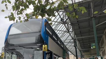 A bus at a bus stop with people queuing to get on.