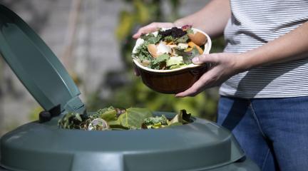 A person putting vegetable cuttings into a compost bin.