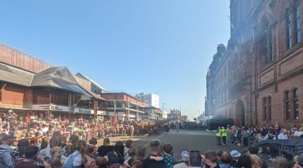 Crowds standing around a rectangular arena watching dinosaurs.