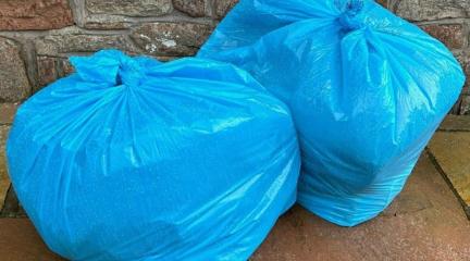 Two blue refuse bags full of rubbish on the ground.