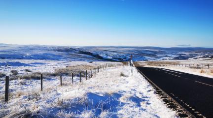 Snowy roadside view down the Hartside Pass valley with bright blue skies