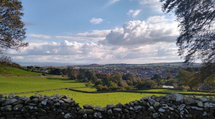 A dry-stone wall with fields and the town of Ulverston beyond.