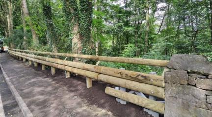 Wooden clad crash barriers on the side of a road with a forest as the backdrop