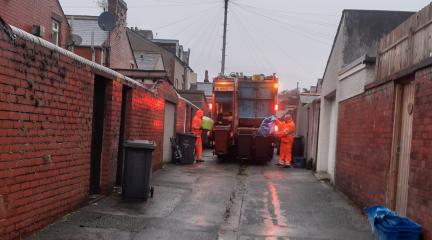 Two crew members in orange overalls loading recycling into the back of a wagon.