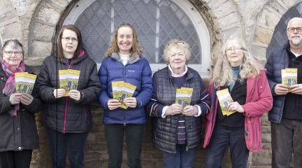 A line-up of five women and one man holding up green leaflets.