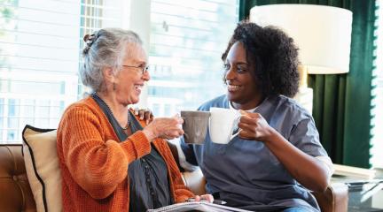 Two women sitting side by side holding mugs and chatting.
