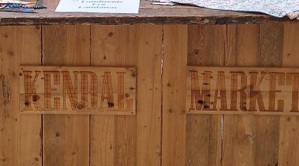 A wooden stall with the words "Kendal Market" on the side.