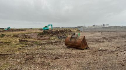 A digger in front of a cleared section of land.