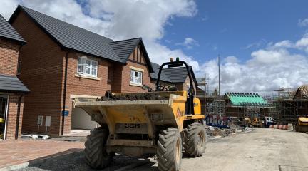 A building site showing a large yellow digger in front of houses being constructed