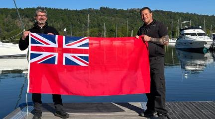 Two Lake Wardens on a jetty at Windermere, holding the Red Ensign flag.