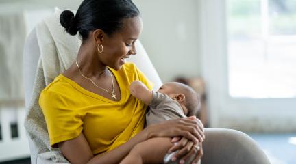 A mother breastfeeding her infant in a chair