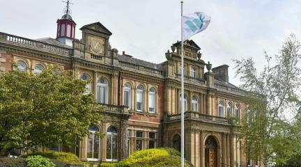 The Grade II Listed building, Penrith Town Hall surrounded by green bushes and flower beds and a Westmorland and Furness flag flying outside