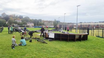 A busy pump track with groups of young people sitting on the grass and people using it.jpg