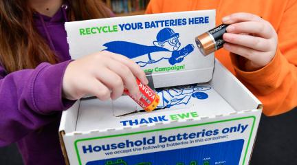 Two schoolchildren placing used batteries in a collection box