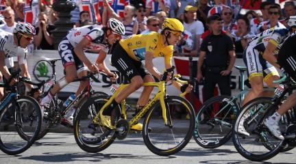 Bradley Wiggins riding a yellow bike and wearing a yellow top and cycling helmet, with spectators in the background