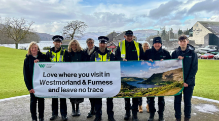 Westmorland and Furness Council and Cumbria Police officers stood holding a banner which reads "Love where you visit and leave no trace" with a mountainous landscape in the background
