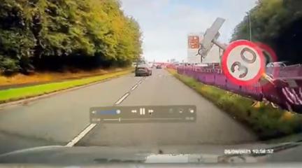 A sign falling into a road, viewed through a car windscreen.