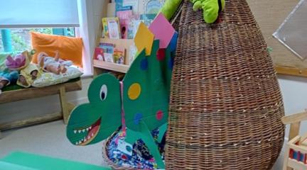 A handmade dinosaur emerging from a wicker egg