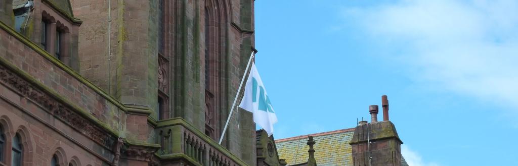 The Westmorland and Furness Council flag flying from a flagpole on a balcony at Barrow Town Hall