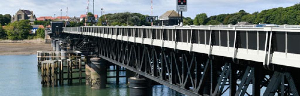 Looking along the railings in the outer edge of Jubilee Bridge over water, with Walney in the background