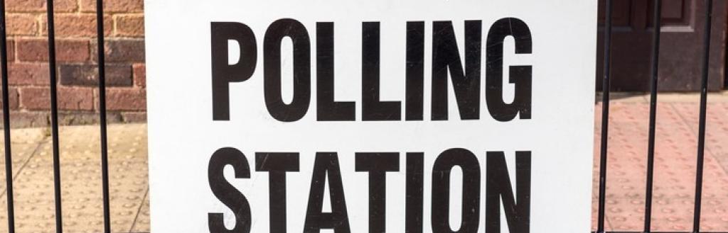 A sign reading "polling station" attached to railings outside the entrance to a building