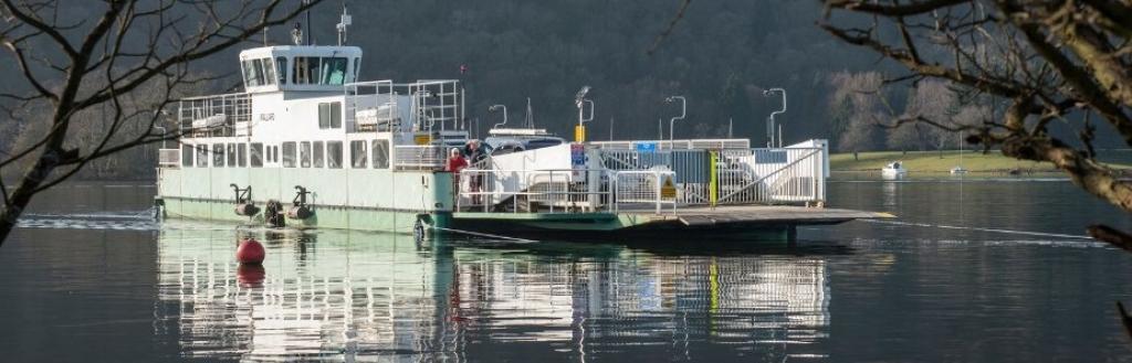 Windermere ferry sailing on calm lake with tree branches to left and right.