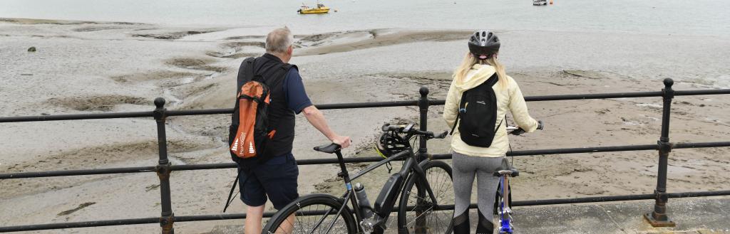 A man and a woman standing with bikes at railings looking over Walney Channel towards Walney
