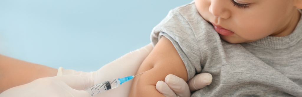 A toddler receiving a vaccine in the right arm from a health professional