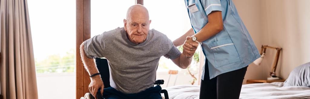 A carer helping an old man into a wheelchair