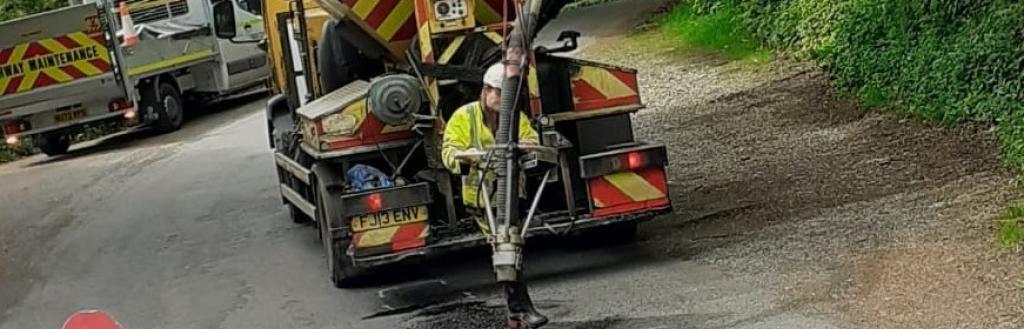 A man at work with a jet-patching machines fixing potholes on a road,
