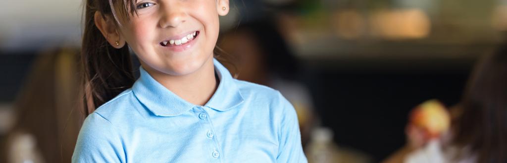 A girl in school uniform holding a school dinner tray, with an apple and banana on top.