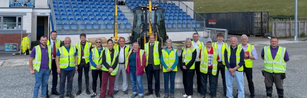 A line of people in yellow high-viz jackets standing in front of seats at a football ground.