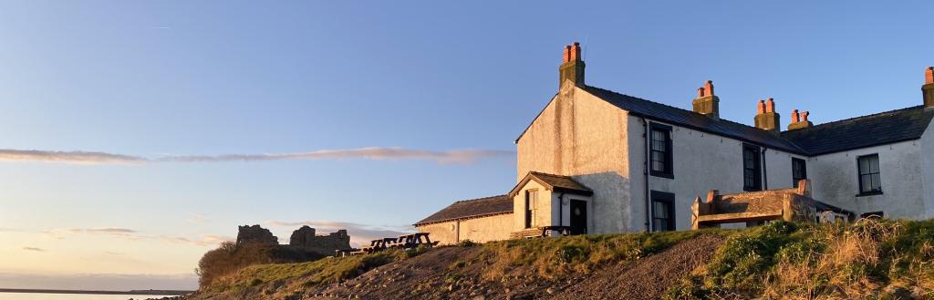 The whitewashed Ship Inn on Piel Island with a stone path leading up to it and a dramatic sky behind