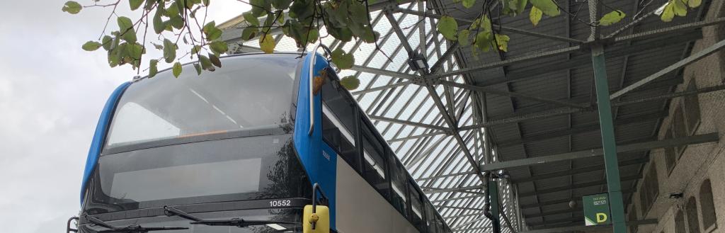 A bus at a bus stop with people queuing to get on.