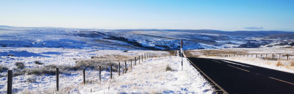 Snowy roadside view down the Hartside Pass valley with bright blue skies