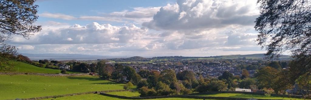 A dry-stone wall with fields and the town of Ulverston beyond.