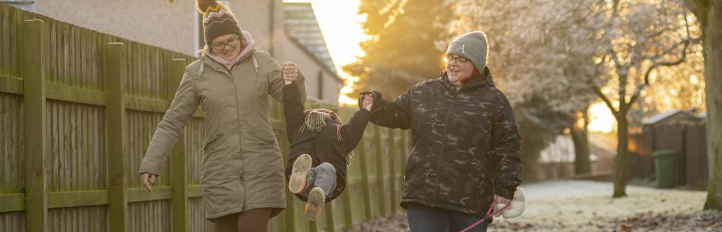 Two women outside swinging their young son between their arms