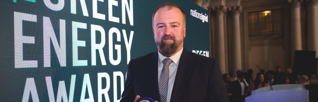 Allan Harty holding Green energy award in front of promotional banner